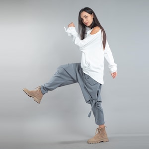May include: A white long-sleeved top with a cold shoulder design, teamed with grey harem trousers and tan boots. The trousers have a unique, loose fit with tie details at the ankles. The outfit is set against a plain grey background.