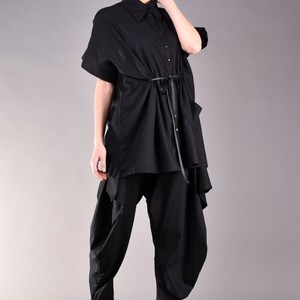 May include: A black shirt with a long, flowing design and a tie at the waist. The shirt is worn with black pants that have a loose, flowing fit.