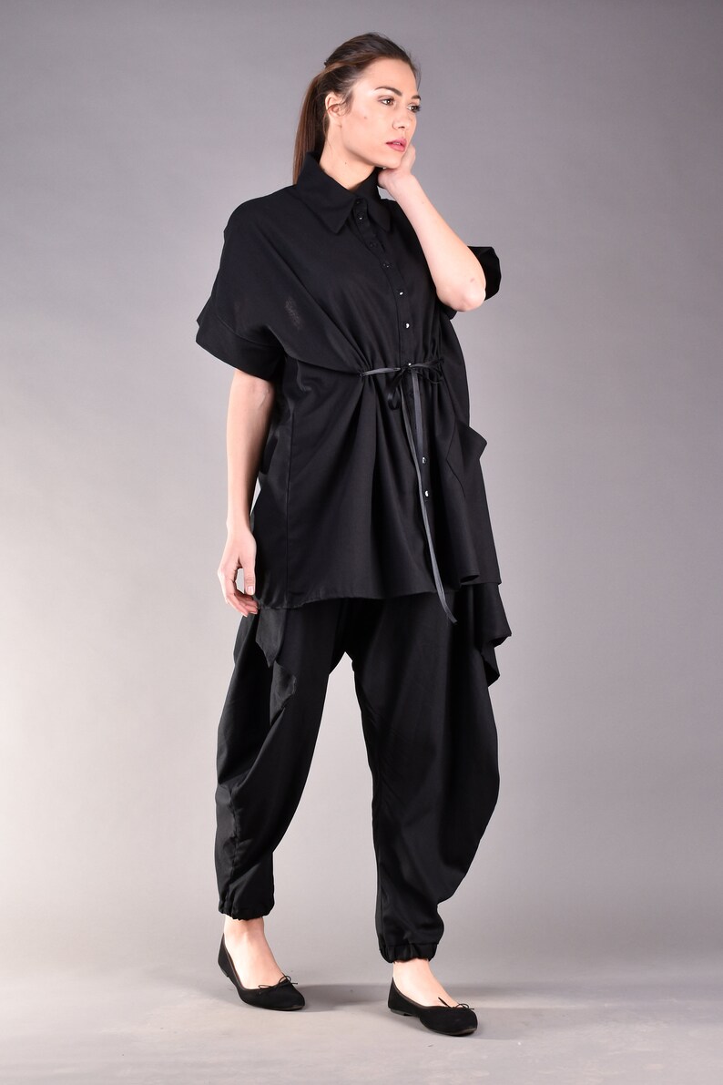 May include: A black shirt with a long, flowing design and a tie at the waist. The shirt is worn with black pants that have a loose, flowing fit.