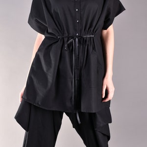 May include: A black oversized shirt with a button-up front and a drawstring waist. The shirt is layered over black pants with a unique design.