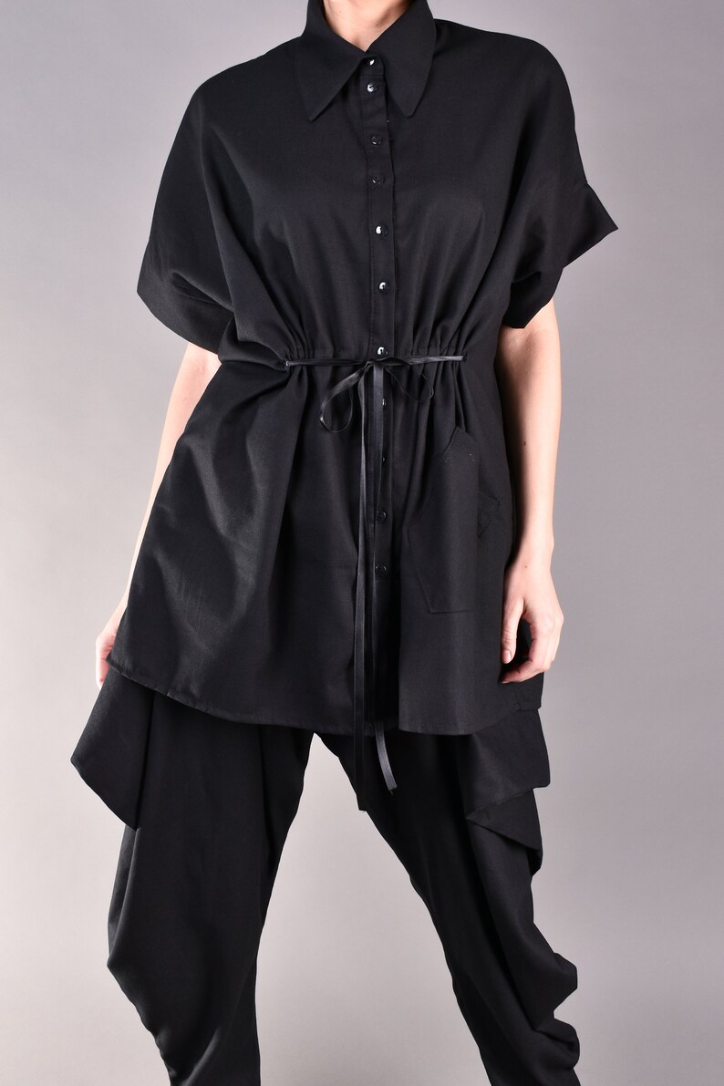 May include: A black oversized shirt with a button-up front and a drawstring waist. The shirt is layered over black pants with a unique design.
