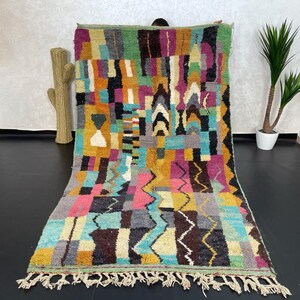 May include: A colourful Moroccan rug with geometric patterns in shades of pink, blue, yellow, green, and brown. The rug has a fringe border and is made of wool.