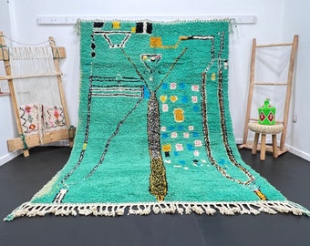May include: A hand-woven Moroccan rug with a geometric design in shades of green, black, white, yellow, and blue. The rug has a fringe border and is made of wool.