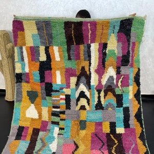 May include: A colourful Moroccan rug with geometric patterns in shades of green, blue, purple, orange, and yellow. The rug is made of wool and has a hand-woven texture.
