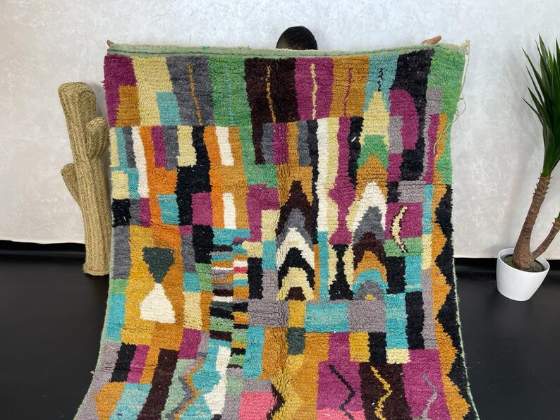 May include: A colourful Moroccan rug with geometric patterns in shades of green, blue, purple, orange, and yellow. The rug is made of wool and has a hand-woven texture.