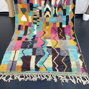 May include: A colourful Moroccan rug with a geometric pattern in shades of blue, pink, yellow, and brown. The rug has a fringe border.