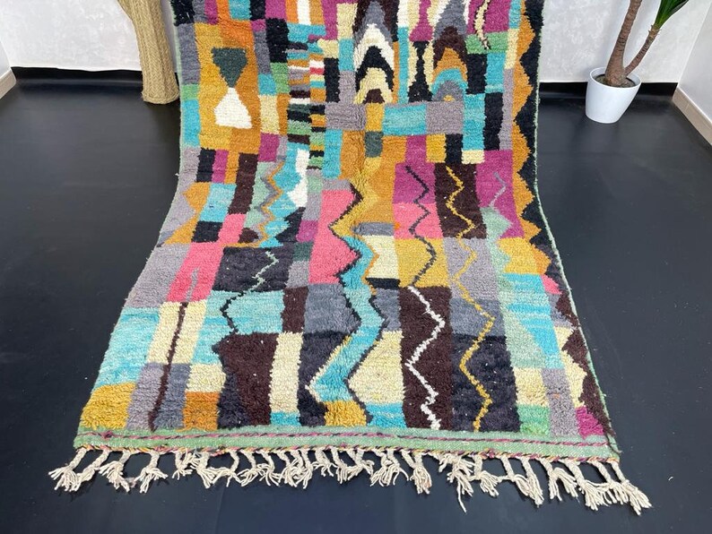 May include: A colourful Moroccan rug with a geometric pattern in shades of blue, pink, yellow, and brown. The rug has a fringe border.