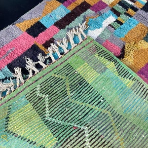 May include: A colourful rug with a geometric pattern in shades of pink, blue, yellow, and green. The rug has a fringe border and is made of wool.