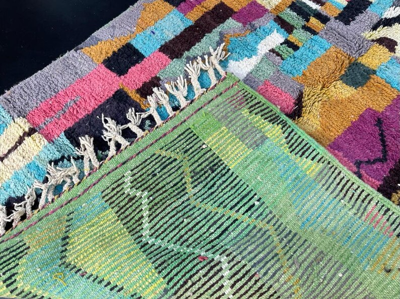 May include: A colourful rug with a geometric pattern in shades of pink, blue, yellow, and green. The rug has a fringe border and is made of wool.