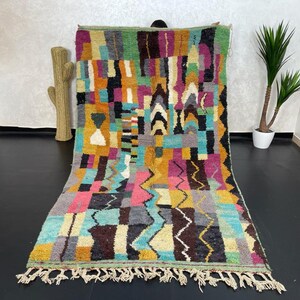 May include: A colourful Moroccan rug with geometric patterns in shades of pink, blue, green, yellow, and brown. The rug has a fringe border and is made of wool.