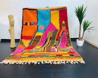 May include: A colorful Moroccan rug with geometric patterns in shades of orange, pink, blue, yellow, and brown. The rug has a fringe border.