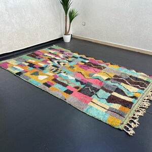 May include: A colourful Moroccan rug with a geometric pattern in shades of blue, green, yellow, pink, and brown. The rug has a fringe border and is made of wool.