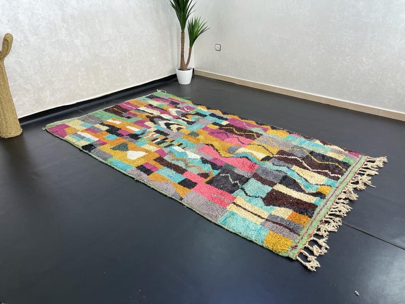 May include: A colourful Moroccan rug with a geometric pattern in shades of blue, green, yellow, pink, and brown. The rug has a fringe border and is made of wool.