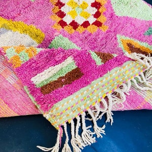 May include: A pink and green patterned rug with white fringe. The rug has a geometric design with a variety of colors, including yellow, orange, brown, and green.