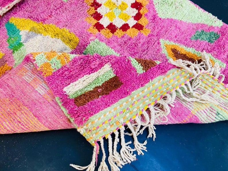 May include: A pink and green patterned rug with white fringe. The rug has a geometric design with a variety of colors, including yellow, orange, brown, and green.