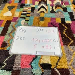 May include: A colourful rug with geometric patterns in shades of pink, blue, yellow, and brown. The rug is 1.54 metres by 2.63 metres and has a B.M. of 816.