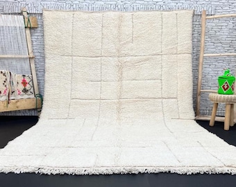 May include: A white Moroccan rug with a geometric pattern. The rug is made of wool and has a fringe border.