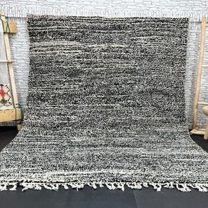 Puede incluir: Una alfombra tejida a mano en blanco y negro con un borde de flecos. La alfombra tiene un patrón tejido texturizado y está hecha con fibras naturales.