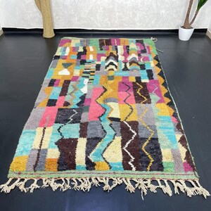 May include: A colourful Moroccan rug with a geometric pattern in shades of blue, green, yellow, pink, and brown. The rug has a fringe border.