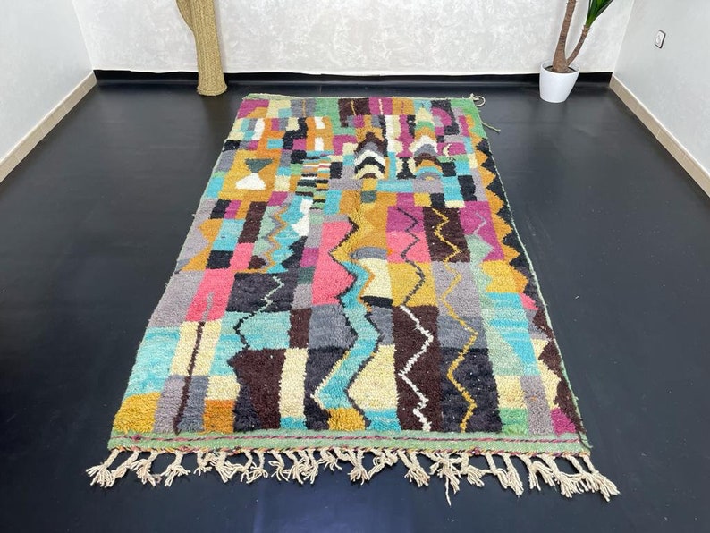 May include: A colourful Moroccan rug with a geometric pattern in shades of blue, green, yellow, pink, and brown. The rug has a fringe border.