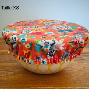 Puede incluir: Una tapa de cuenco de tela con estampado floral en tonos naranja, rosa, azul y verde. La tapa está sobre un cuenco amarillo. El texto "Taille XS" es visible en la esquina superior izquierda de la imagen.