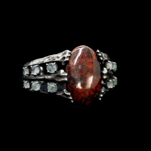 May include: A silver ring with a large, oval-shaped red gemstone surrounded by smaller, clear gemstones.