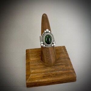May include: A silver ring with a green gemstone set in a triangular bezel. The ring is decorated with small silver beads around the bezel.