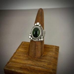 May include: A silver ring with a green gemstone set in a triangular bezel. The ring is decorated with small silver beads around the bezel.