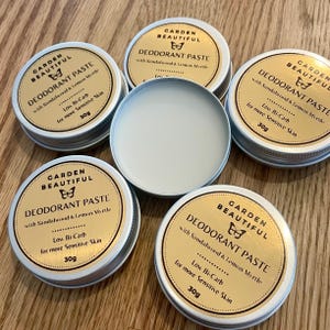 May include: Five small, silver, round tins with gold lids. Each tin contains a natural deodorant paste and has a label that reads "Garden Beautiful Deodorant Paste with Sandalwood & Lemon Myrtle. Low Bi-Carb for more Sensitive Skin. 30g."