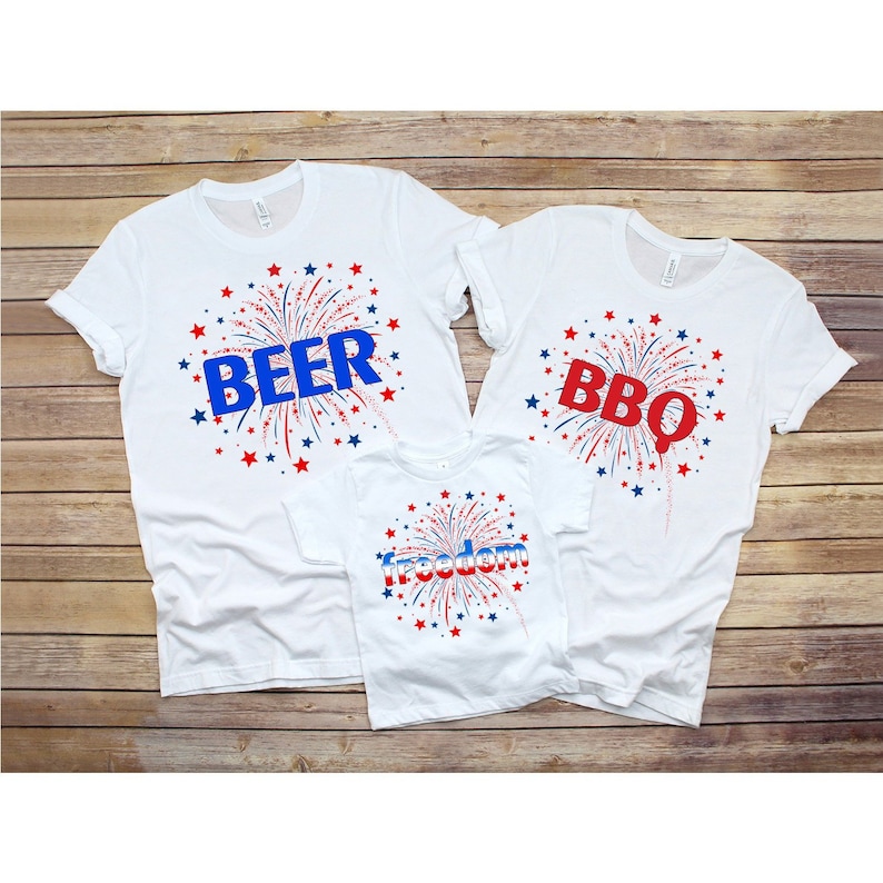 May include: Three white t-shirts with red, white, and blue firework designs. The shirts have the words "Beer", "BBQ", and "Freedom" printed on them.