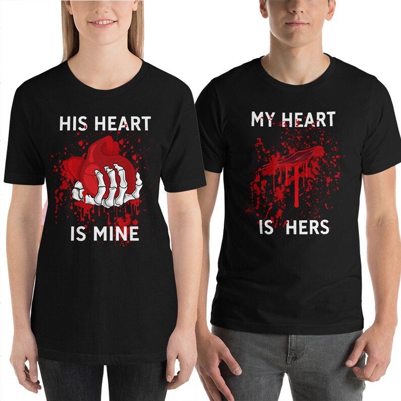 May include: Two black t-shirts with a graphic print of a bloody heart. The text on the first shirt reads "His heart is mine". The text on the second shirt reads "My heart is hers".