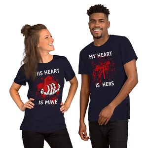May include: Two navy blue t-shirts with a graphic print of a skeleton hand holding a red heart. The text on the shirts reads "His heart is mine" and "My heart is hers".