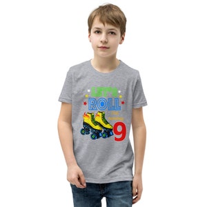 May include: A grey t-shirt with the words "LET'S ROLL I'M TURNING 9" and a graphic of yellow roller skates. The design includes colourful stars and the number 9 in red. The shirt is worn by a young person.