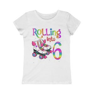 Puede incluir: Camiseta blanca con un gr&aacute;fico de arco&iacute;ris que dice "Rolling into 6" con un par de patines de ruedas de arco&iacute;ris.