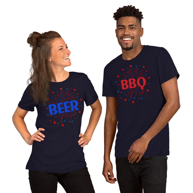 May include: Two navy blue t-shirts with red and blue firework designs. One shirt says "BEER" in blue letters and the other says "BBQ" in red letters.