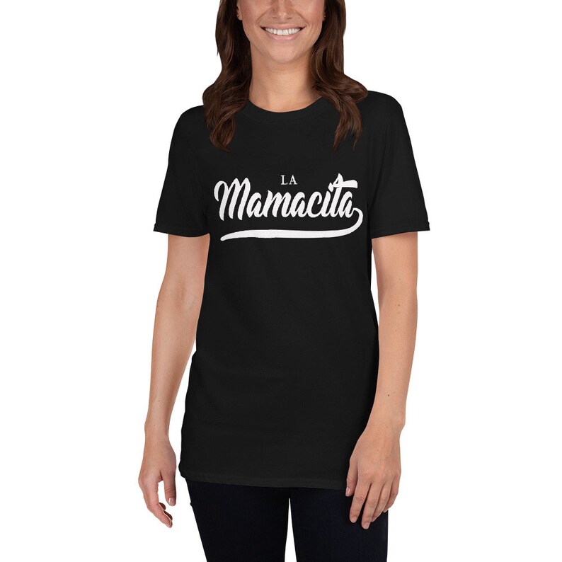 Puede incluir: Camiseta negra con texto blanco que dice "LA Mamacita" en una fuente cursiva.