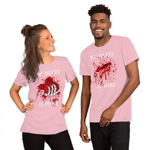 May include: Two pink t-shirts with a graphic print of a bloody heart and a skeleton hand. The text on the shirts reads "His heart is mine" and "My heart is hers".