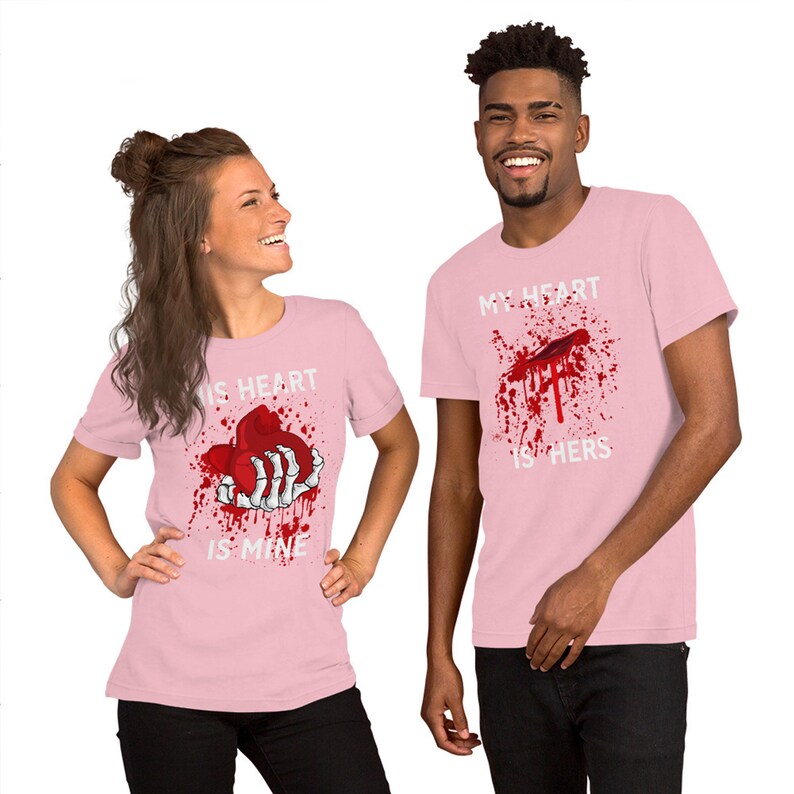 May include: Two pink t-shirts with a graphic print of a bloody heart and a skeleton hand. The text on the shirts reads "His heart is mine" and "My heart is hers".
