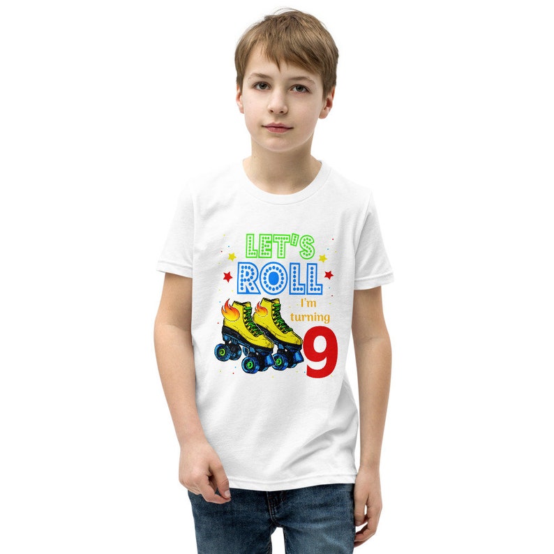 May include: White t-shirt featuring the text "Let's Roll I'm turning 9" and a graphic of yellow roller skates with blue wheels and flames. The number 9 is in red. The shirt is for a child.
