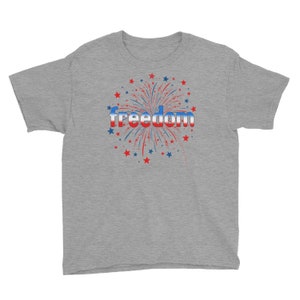 May include: A heather grey youth t-shirt with a red, white, and blue firework graphic and the word "freedom" in a red, white, and blue gradient.