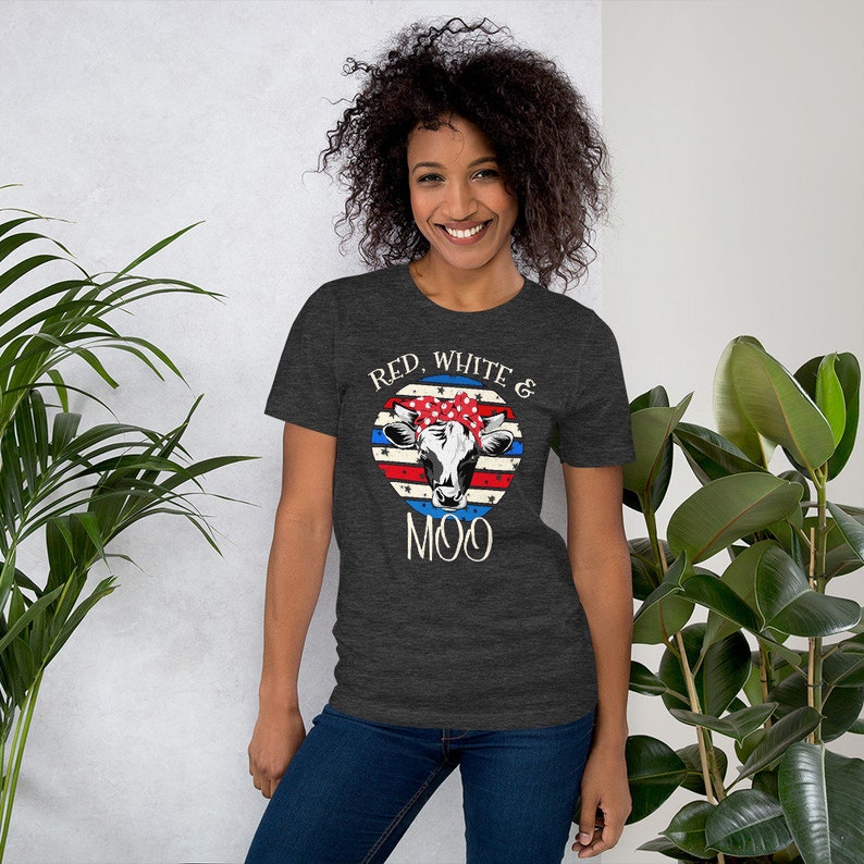Może przedstawiać: Szary t-shirt z nadrukiem w kolorze czerwonym, białym i niebieskim, przedstawiającym amerykańską flagę z krową w czerwono-biało-niebieskiej bandanie. Na koszulce widnieje napis "Red, White & Moo".