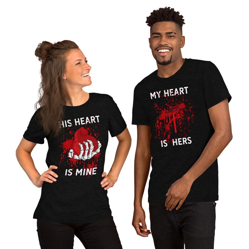 May include: A couple's matching t-shirts with a graphic of a bloody hand holding a heart. The woman's shirt says "His heart is mine" and the man's shirt says "My heart is hers".