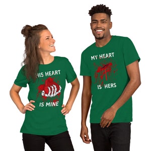 May include: Two green t-shirts with a graphic print of a bloody heart and the text "His heart is mine" and "My heart is hers".