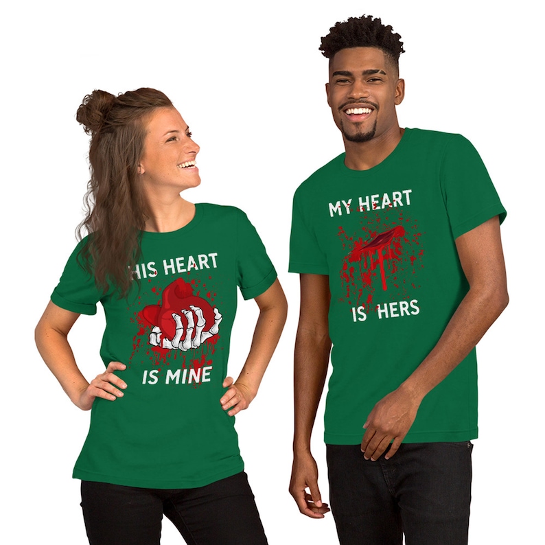 May include: Two green t-shirts with a graphic print of a bloody heart and the text "His heart is mine" and "My heart is hers".