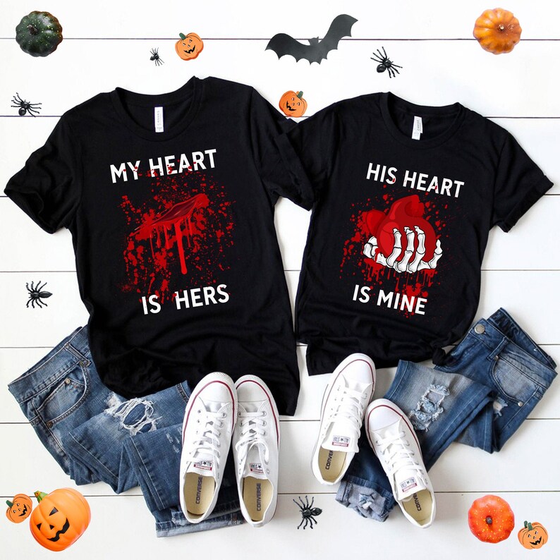May include: Two black t-shirts with a Halloween theme. The left shirt says "My heart is hers" with a bloody heart. The right shirt says "His heart is mine" with a skeleton hand holding a bloody heart.