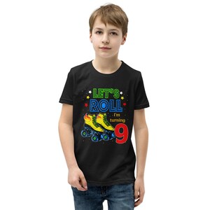 May include: Black t-shirt with the text "Let's Roll, I'm turning 9" in a colourful graphic. The graphic includes yellow roller skates with blue wheels and flames. The shirt is worn by a young person.