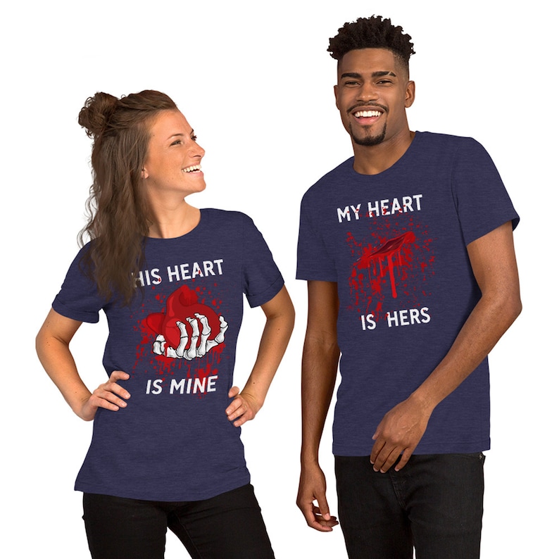 May include: Two navy blue t-shirts with a graphic print of a bloody heart. The text on the left shirt reads "His heart is mine". The text on the right shirt reads "My heart is hers".