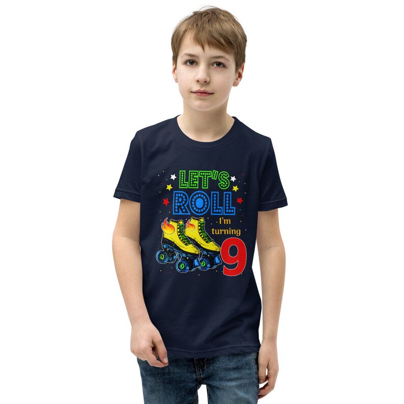 May include: A navy blue t-shirt featuring the text "Let's Roll, I'm turning 9". The graphic includes yellow roller skates with blue wheels and the number 9 in red. The shirt is worn by a young person.