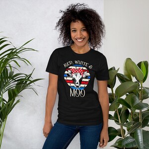 Może przedstawiać: Czarny T-shirt z grafiką czerwono-biało-niebieskiej krowy. Krowa nosi czerwoną, białą i niebieską chustkę. Na koszulce nadrukowany jest napis "Red, White & Moo".