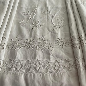 Può includere: Tessuto di lino bianco con le iniziali ricamate "A" e "C". Il tessuto presenta intricati intagli floreali e bordi decorativi. Il design include una serie di motivi floreali ritagliati e un bordo all'uncinetto.